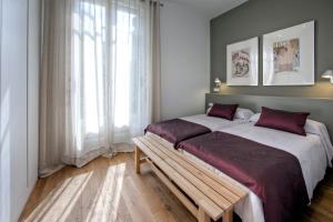 two beds in a room with a bench and a window at Habitat Apartments Rambla Deluxe in Barcelona