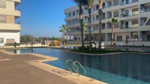 ブズニカにあるSpécial CAN 2025,louer votre appt sur Bouznika entre Rabat & Casaのヤシの木が茂る建物の前にあるスイミングプール