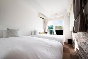 two beds in a white room with a window at WITH SEA Nakama in Onna
