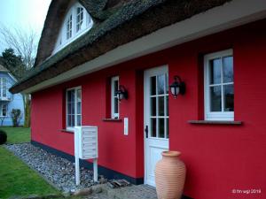 ein rotes Haus mit einer weißen Tür und einer Vase in der Unterkunft Landhaus Uhlenhof 4 in Groß Zicker