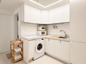 a white kitchen with a washing machine and a microwave at 3-Min Walk from Achasan Station, 2-Bedroom Bali Mood Stay with Hinoki Aroma in Seoul