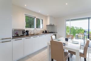 a white kitchen with a table and a dining room at Le Petit Bois évasion nature entre Genève&Annecy in Copponex