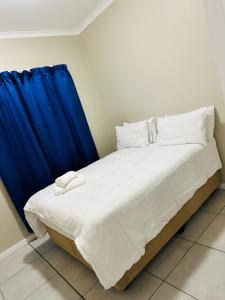 a bed with white sheets and a blue curtain at One on Heather Midrand 