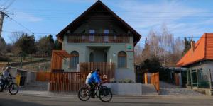 a person riding a bike in front of a house at Bagoly-kő Panzió - Mátra Túraközpont in Parádsasvár