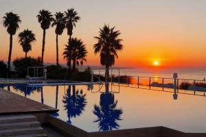 a pool with palm trees in front of a sunset at Hotel Cascais Miragem Health & Spa in Cascais