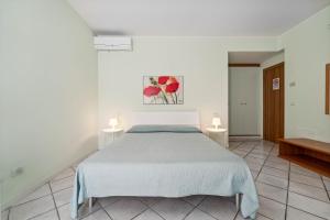 a white bedroom with a bed and two tables at Green Village Accommodations in Colico
