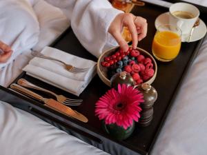 a tray of fruit on a bed with a person reaching for a flower at Sofitel Legend The Grand Amsterdam in Amsterdam
