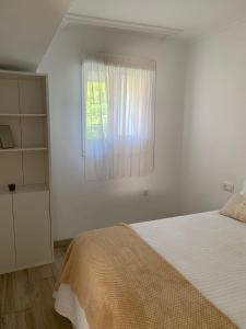 a white bedroom with a bed and a window at Brisa Azul in Moaña