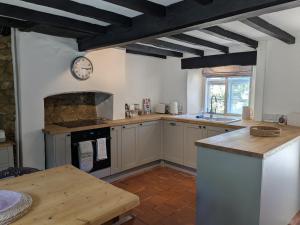 a kitchen with white cabinets and a clock on the wall at Period Thatched Cottage Towcester in Towcester