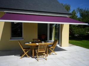 a table and chairs on a patio with a purple awning at Les jardins de kerarzic in Ploubazlanec