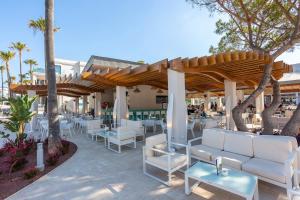 a patio at a resort with white furniture and trees at Hipotels Barrosa Park in Chiclana de la Frontera