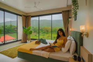 a woman sitting on a bed reading a book at EKOSTAY Luxe - Harmony Heights in Alibaug