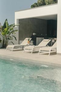 eine Gruppe weißer Liegestühle neben einem Pool in der Unterkunft Alda & Aljosía in Chiclana de la Frontera