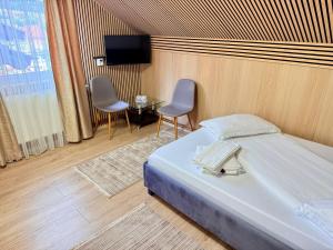 a bedroom with a bed and two chairs and a tv at Pensiunea Monady in Zărneşti