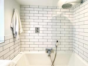 a white bathroom with a tub and white tiles at Bertie by The Suffolk Cottage Collection in Chillesford +19 photos