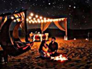 a couple sitting around a fire on the beach at night at Luxury Diaries Camp in Merzouga