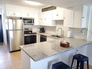 Una cocina con gabinetes blancos y un refrigerador de acero inoxidable. en Ocean View 2 Bed, 2 bath, Steps to the Beach - Spanish Trace 240, en Coquina Gables