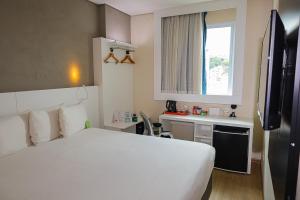 a bedroom with a large white bed and a kitchen at Esuites Virgínia Luxemburgo in Belo Horizonte