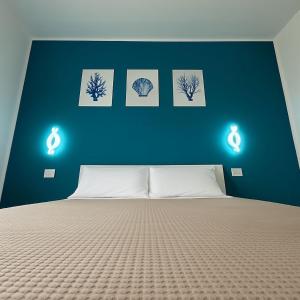 a bedroom with a blue wall with a bed and three pictures at La Conchiglia Apartment Villa Margi in Santo Stefano di Camastra