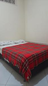 a bed with a red plaid blanket on it at Kitnet jardim Campomar in Rio das Ostras