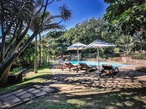 a swimming pool with two chairs and umbrellas at Beachfront petfriendly cottage in Zinkwazi Beach