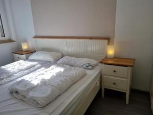 ein Bett mit weißer Bettwäsche und zwei Nachttischen mit zwei Lampen in der Unterkunft Ferienhaus Ohrenqualle in Dornum