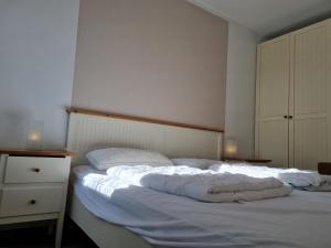 Schlafzimmer mit einem Bett mit weißer Bettwäsche und einer Kommode in der Unterkunft Ferienhaus Ohrenqualle in Dornum