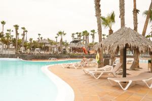 a resort with a swimming pool and chairs and palm trees at Oasis Dunas Corralejo in Corralejo