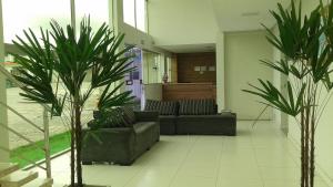 a living room with two couches and two palm trees at Hotel Vento Sul in Teixeira de Freitas