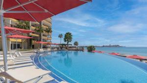 a swimming pool with chairs and umbrellas next to the ocean at The Great Escape Modern Oceanfront in Puerto Peñasco