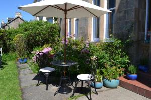 uma mesa e cadeiras sob um guarda-sol num jardim em Maybank Guest House em Helensburgh