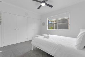 a white bedroom with a bed and a ceiling fan at Bikinis & Martinis in Vincentia +12 photos