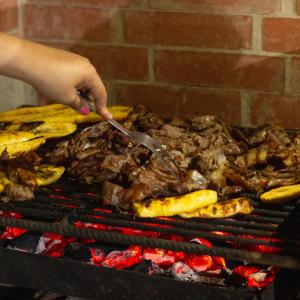 a person cooking meat on a grill with a spoon at Refugio, Casa de la Playa in Manaure