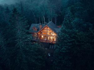 Ein Haus mit eingeschaltetem Licht mitten in einem Wald in der Unterkunft Chalet Mazama - Private Lake - Hot Tub - 16P in Wentworth-Nord