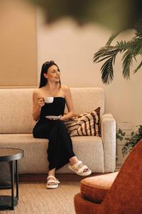 a woman sitting on a couch holding a cup of coffee at Leonardo Boutique Hotel Larnaca in Larnaca