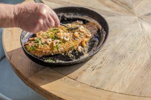 a person cooking food in a pan on a wooden table at Harbour Hotel & Spa Christchurch in Christchurch
