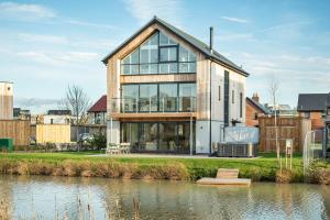 a house with large glass windows next to a river at Everdene OI14 Lakeside Property with Hot Tub at Silverlake Dorset in Warmwell