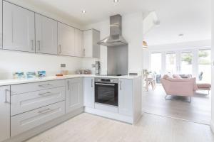 a white kitchen with white cabinets and a pink chair at 5 Parc Delfryn in Benllech