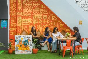 Un grupo de mujeres sentadas en una mesa frente a una pared. en Zostel Pushkar, en Pushkar