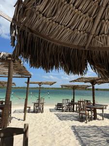 a beach with tables and chairs and a straw umbrella at O Caminho das Dunas in Jericoacoara