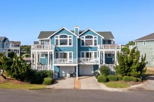 a large blue house with balconies and trees at White Dolphin Left in Corolla