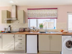 une cuisine avec des armoires blanches, un évier et une fenêtre dans l'établissement Harebell Cottage, à Addlethorpe