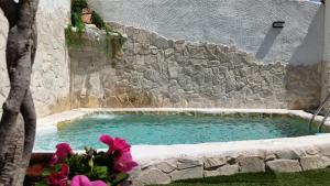 a swimming pool with a stone wall and purple flowers at Casa Los Templarios, Puy du fou Toledo in Burujón