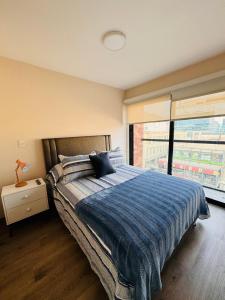a bedroom with a bed with a blue blanket and a window at Monterrico Polo Aparts 19 - Dpto de Estreno con Balcon frente Embajada USA in Lima