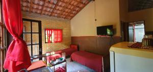 Una sala de estar con un sofá rojo y un televisor. en Tahoma Chale Rustico côr Café e vermelho Prumirim Paraiso, en Ubatuba