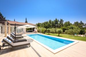 a swimming pool with chairs and a house at Villa Stella - heated pool, jacuzzi & sauna in Šibenik