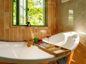 a bath tub with a glass of wine and a window at JM Villas Tropical Khem Beach in Phu Quoc