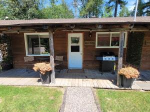 a wooden cabin with a white door and a grill at Pine Ridge Park Campground in Pembroke