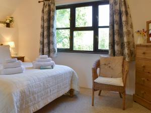 una camera da letto con un letto, una sedia e una finestra di Clematis Cottage a Holsworthy