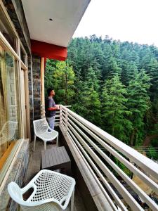 a man standing on a balcony looking at the forest at Decent Stays in Shimla